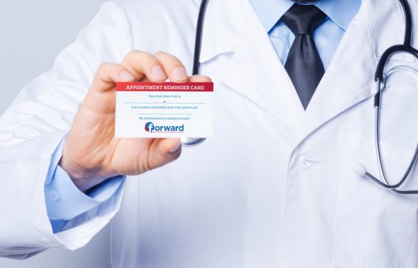 Doctor holding business card. Cheerful mature doctor showing his business card and smiling while standing against grey background